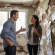 An insurance adjuster and homeowner having a tense discussion in a room with walls ripped open, showing water-stained insulation